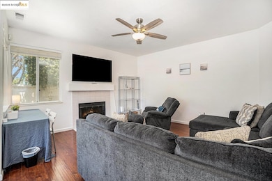 Living area featuring a ceiling fan, a tile fireplace, and dark wood-style flooring