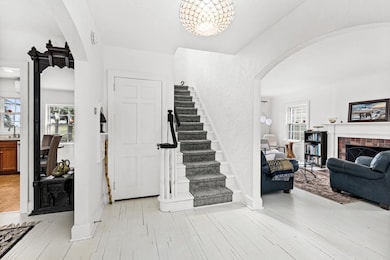 Entrance foyer with a fireplace, light wood-style floors, arched walkways, baseboards, and stairway