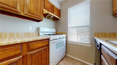 Kitchen featuring dishwasher, light tile patterned floors, tile countertops, and white range with gas cooktop