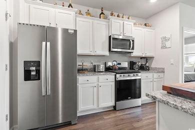 Kitchen featuring stainless steel appliances, dark wood finished floors, white cabinetry, and light stone counters