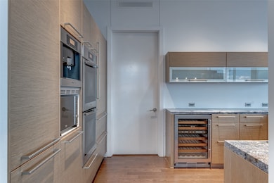 Kitchen featuring light wood-type flooring, beverage cooler, modern cabinets, stainless steel double oven, and light stone counters