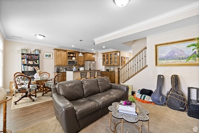 Living room with crown molding, stairs, light wood-style floors, and wet bar