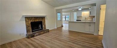 Unfurnished living room featuring wood finished floors, a stone fireplace, and ceiling fan