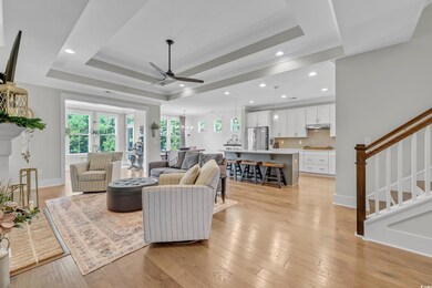Living area featuring a tray ceiling, ceiling fan, stairs, light wood-type flooring, and recessed lighting