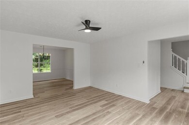 Empty room with light wood-type flooring, stairway, a ceiling fan, a textured ceiling, and a chandelier