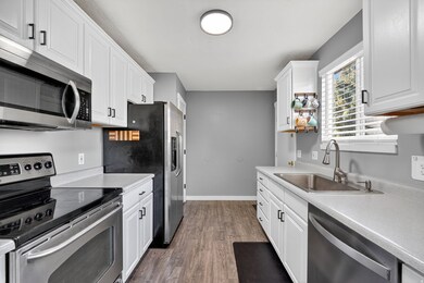 Kitchen with appliances with stainless steel finishes, dark wood-style flooring, light countertops, and white cabinets. Refrigerator is included with sale.