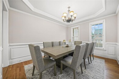 Dining area with a chandelier, wood finished floors, a raised ceiling, a wainscoted wall, and ornamental molding