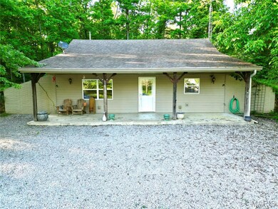 View of front facade with roof with shingles, view of scattered trees, and a porch