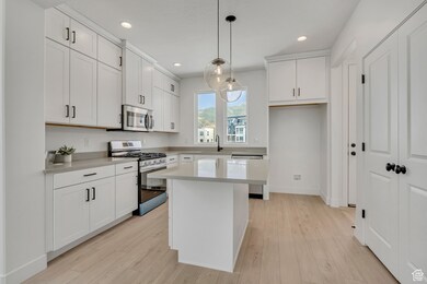 Kitchen featuring appliances with stainless steel finishes, white cabinets, hanging light fixtures, a center island, and light wood finished floors