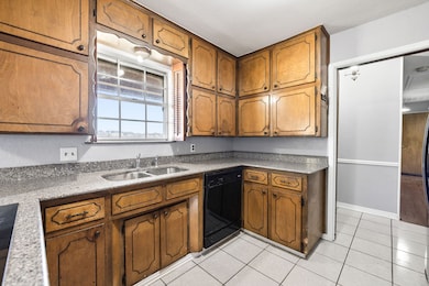 Kitchen featuring brown cabinets, black dishwasher, light stone counters, and light tile patterned floors
