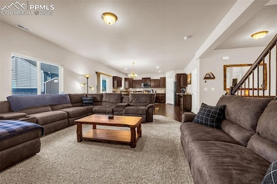 Living area featuring a chandelier, stairs, dark wood-style flooring, and a textured ceiling