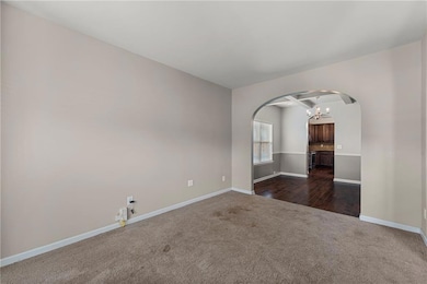Spare room with arched walkways, dark carpet, baseboards, and a chandelier