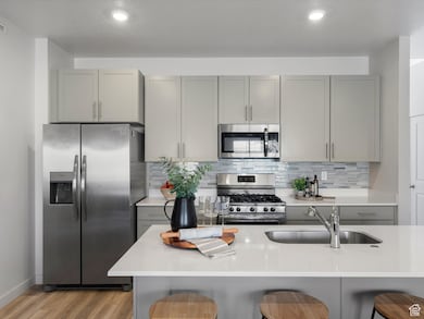 Kitchen featuring gray cabinetry, stainless steel appliances, tasteful backsplash, light stone counters, and a textured ceiling