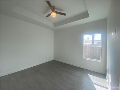 Spare room with a tray ceiling, a ceiling fan, and dark wood-style flooring