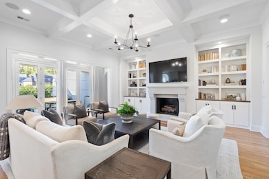 Living area featuring light wood finished floors, recessed lighting, a fireplace with raised hearth, beam ceiling, and a chandelier