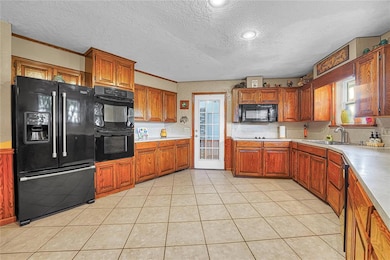 Kitchen with black appliances, a sink, a textured ceiling, solid wood cabinets, and light countertops