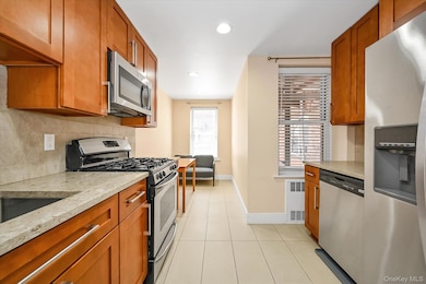 Kitchen featuring stainless steel appliances, light stone countertops, tasteful backsplash, recessed lighting, and brown cabinets