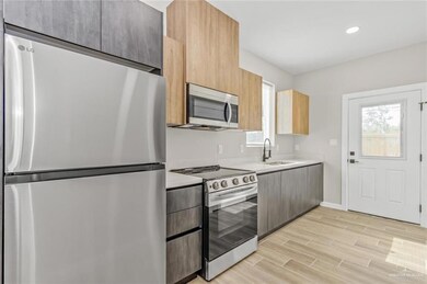 Kitchen with stainless steel appliances, a sink, modern cabinets, light countertops, and light wood-style flooring