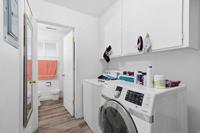 Washroom with light wood finished floors, cabinet space, washer and clothes dryer, and electric panel