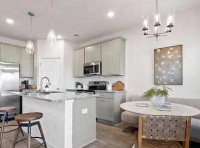 Kitchen with gray cabinetry, stainless steel appliances, light stone countertops, a chandelier, and an island with sink