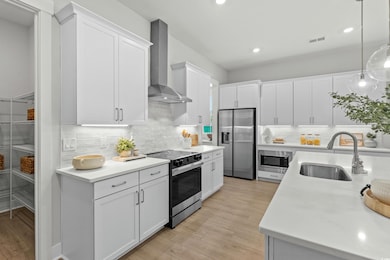 Kitchen featuring appliances with stainless steel finishes, tasteful backsplash, hanging light fixtures, wall chimney exhaust hood, and recessed lighting