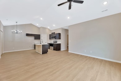 Kitchen featuring open floor plan, a kitchen island with sink, stainless steel appliances, light wood-style flooring, and pendant lighting