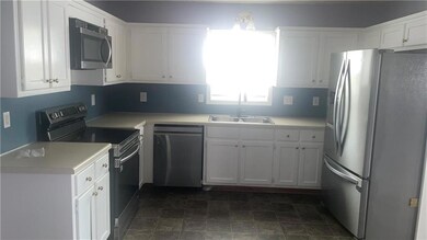Kitchen featuring stainless steel appliances, white cabinetry, light countertops, and stone finish flooring