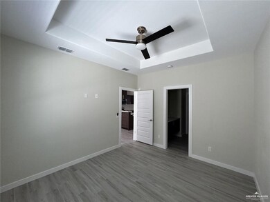 Unfurnished bedroom featuring a raised ceiling, wood finished floors, baseboards, and ceiling fan