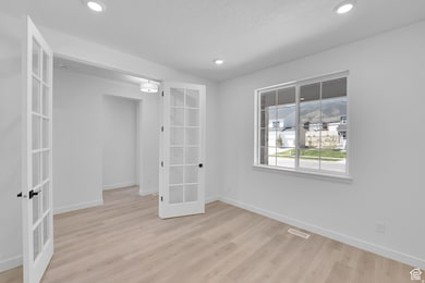 Empty room with french doors, light wood-style flooring, and recessed lighting