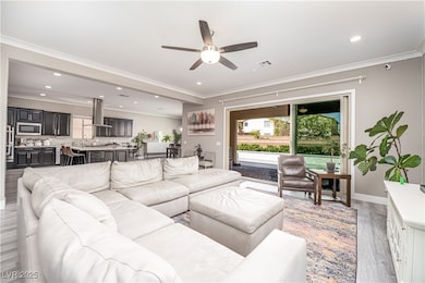 10 ft ceilings! Living area featuring light luxury vinyl plank flooring, crown molding, ceiling fan, and recessed lighting. Oversized slider to backyard.
