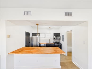Kitchen with appliances with stainless steel finishes, pendant lighting, dark cabinetry, butcher block counters, and a peninsula