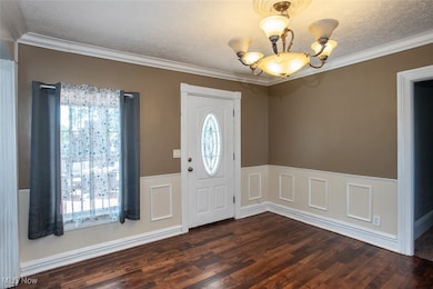 Entrance foyer featuring crown molding, wainscoting, a textured ceiling, a chandelier, and a decorative wall