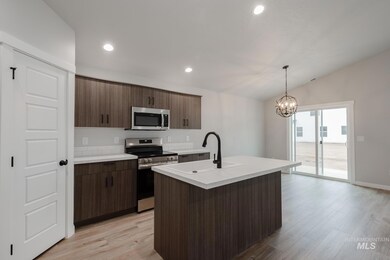 Kitchen with light countertops, stainless steel appliances, a kitchen island with sink, light wood-style floors, and dark brown cabinets