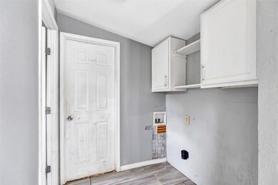 Laundry area with upper white cabinets for storage, a connection for a washer and dryer, and a door leading outside. The walls are painted in a neutral gray, and the floor features light tiles.