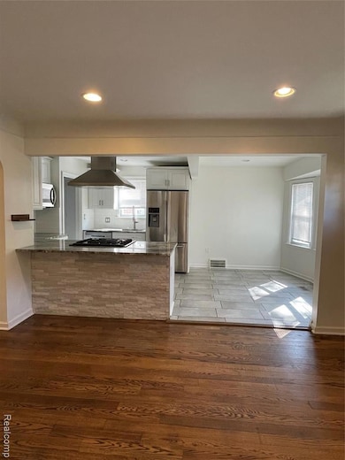 Kitchen featuring white cabinetry, stainless steel refrigerator with ice dispenser, dark wood finished floors, dark stone countertops, and ventilation hood