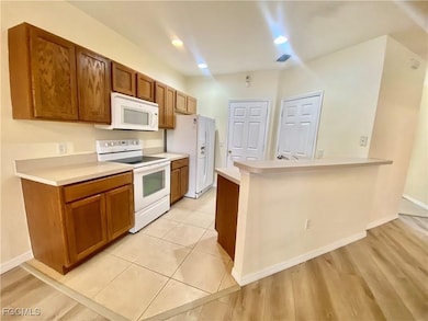Kitchen featuring white appliances, light countertops, a peninsula, brown cabinets, and recessed lighting