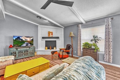 Living room with a textured ceiling, beam ceiling, wood finished floors, ceiling fan, and a fireplace