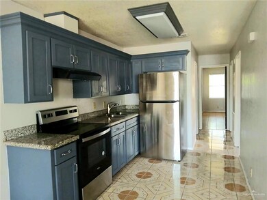 Kitchen featuring stainless steel electric range and refrigerator appliances, under cabinet range hood, blue cabinetry, patterned floors, dark granite counters.