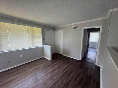 Unfurnished bedroom with ornamental molding, a textured ceiling, dark wood-style floors, and a closet