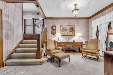Sitting room with wallpapered walls, ornamental molding, carpet floors, a chandelier, and stairs