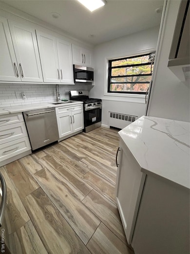 Kitchen with light wood-style floors, decorative backsplash, range, white cabinetry, and stainless steel dishwasher
