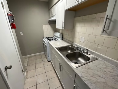 Kitchen featuring light tile patterned floors, white range with gas stovetop, under cabinet range hood, decorative backsplash, and a sink
