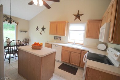 Kitchen with white appliances, light tile patterned floors, ceiling fan with notable chandelier, vaulted ceiling, and sink