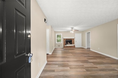 Unfurnished living room with a ceiling fan, wood finished floors, a textured ceiling, and a fireplace