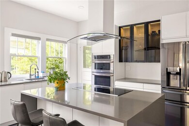 Kitchen with refrigerator with ice dispenser, stainless steel double oven, island exhaust hood, black electric stovetop, and modern cabinets