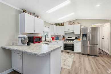 Kitchen featuring stainless steel appliances, lofted ceiling, light countertops, a peninsula, and light wood finished floors