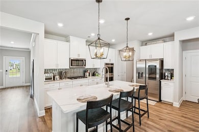 Kitchen featuring stainless steel appliances, a chandelier, decorative backsplash, a center island with sink, and a breakfast bar area