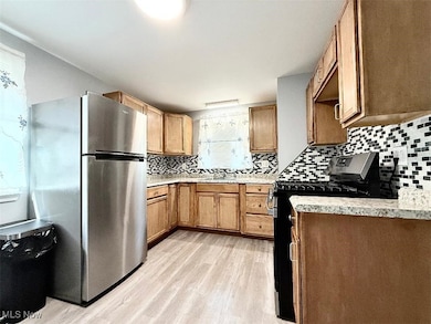 Kitchen featuring freestanding refrigerator, gas range, tasteful backsplash, laminate wood finished floors, and brown cabinets