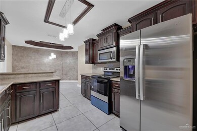 Kitchen featuring appliances with stainless steel finishes, dark brown cabinets, light tile patterned floors, light countertops, and an inviting chandelier