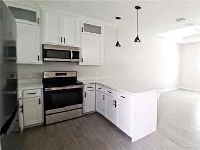 Kitchen with stainless steel appliances, glass insert cabinets, a peninsula, and white cabinetry